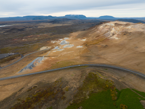 Aerial view of the geothermal field s otherworldly terrain with steam rising from vents and a road winding through the landscape Reykjahl&iacute;&eth; &THORN;ingeyjarsveit Iceland.