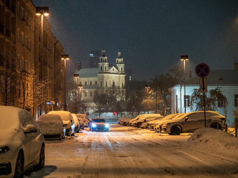 View of the Church of St. Catherine illuminated at night during a winter snowfall with snow covered cars parked along a street in Vilnius Vilnius County Lithuania. View of the Church of St. Catherine illuminated at night during a winter snowfall with snow covered cars parked along a street in Vilnius Vilnius County Lithuania.