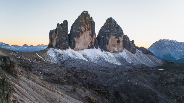 Aerial view of the iconic Tre Cime di Lavaredo peaks with snow dusted rocky slopes under a clear twilight sky in the Dolomites Auronzo di Cadore Veneto Italy. Aerial view of the iconic Tre Cime di Lavaredo peaks with snow dusted rocky slopes under a clear twilight sky in the Dolomites Auronzo di Cadore Veneto Italy.