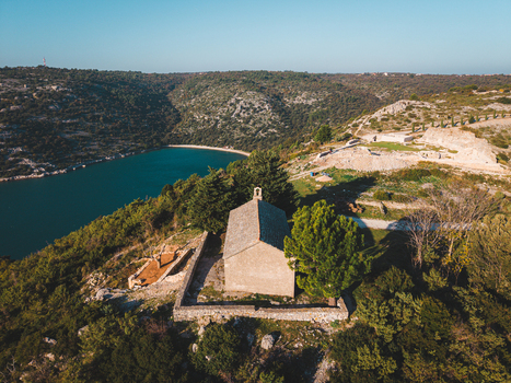 Aerial view of a quaint church perched atop a hill overlooking a serene lake contrasting with the rugged terrain and lush greenery Rakalj Istria County Croatia.