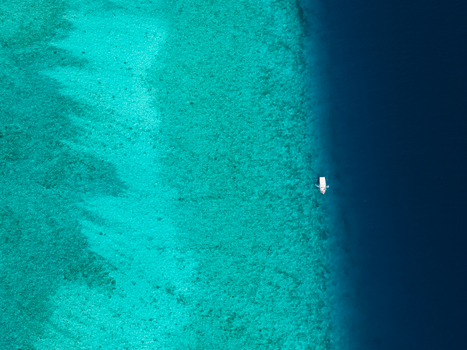Aerial view of a lone boat sailing on the turquoise waters contrasting with the deep blue sea Vashafaru Island Thiladhummathi Atoll Maldives.