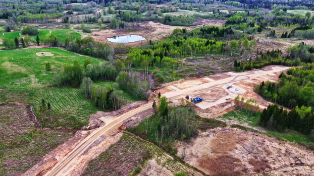 Aerial view of a newly constructed dirt access road for wind turbine maintenance winding through rural green fields and forests in Latvija. Aerial view of a newly constructed dirt access road for wind turbine maintenance winding through rural green fields and forests in Latvija.