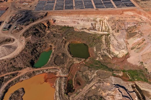 Aerial view of an open pit mine featuring discolored industrial waste ponds in shades of green brown and orange surrounded by barren mining terrain in Welkom Free State South Africa.