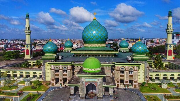 Aerial view of An Nur Great Mosque with its distinctive green domes and minarets surrounded by gardens and the city skyline in Pekanbaru Riau Indonesia. Aerial view of An Nur Great Mosque with its distinctive green domes and minarets surrounded by gardens and the city skyline in Pekanbaru Riau Indonesia.