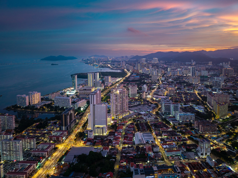 George Town Malaysia 22 September 2026 Aerial view of the George Town cityscape at twilight featuring illuminated skyscrapers coastal roads and the sea under a sunset sky.