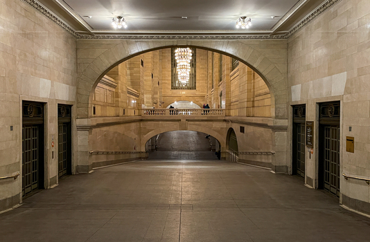 View of the historic stone arches and elegant chandeliers inside Grand Central Terminal with elevators and distant figures New York New York United States. View of the historic stone arches and elegant chandeliers inside Grand Central Terminal with elevators and distant figures New York New York United States.