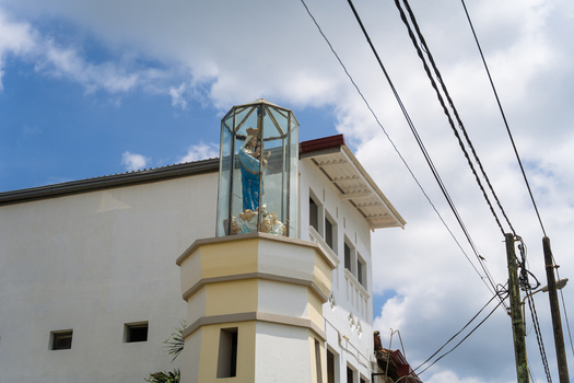 View of the statue of Our Lady of Matara in a glass enclosure atop a white building under a blue sky with clouds in Matara Southern Province Sri Lanka.