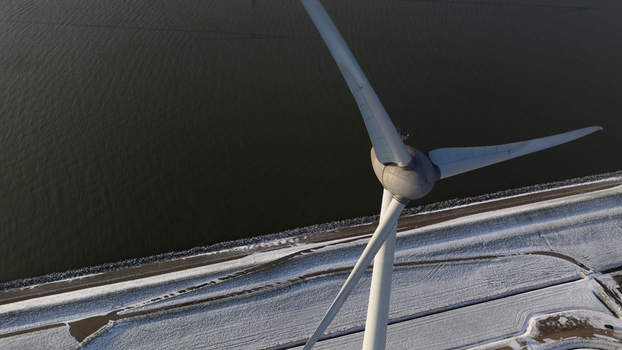 Aerial view of a large wind turbine standing over a snow covered landscape and a dike along the water Espel Flevoland Netherlands. Aerial view of a large wind turbine standing over a snow covered landscape and a dike along the water Espel Flevoland Netherlands.
