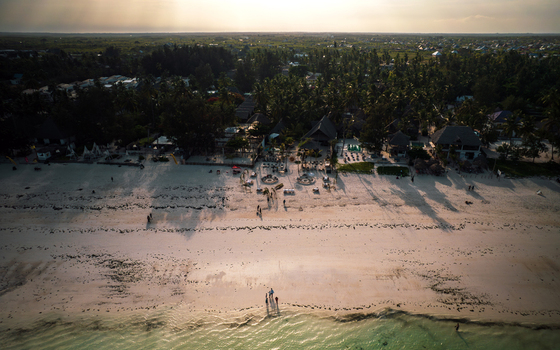 Aerial view of the sun kissed beach where the turquoise ocean meets the tan sand fringed by lush green palm trees Paje Unguja South Region Tanzania. Aerial view of the sun kissed beach where the turquoise ocean meets the tan sand fringed by lush green palm trees Paje Unguja South Region Tanzania.