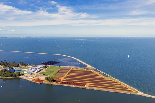 Aerial view of circular floating round solar panels located in the IJsselmeer near the coast with agricultural fields and industrial facilities in Andijk Noord Holland Netherlands. Aerial view of circular floating round solar panels located in the IJsselmeer near the coast with agricultural fields and industrial facilities in Andijk Noord Holland Netherlands.