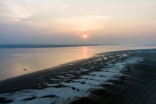 Aerial view of the Padma River at sunset with sandy banks small pools of water and a lone boat in Rajshahi Rajshahi Division Bangladesh.