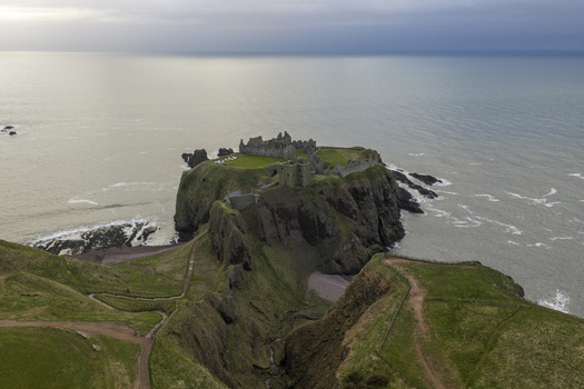 Aerial view of Dunnottar Castle ruins on a rocky headland surrounded by the North Sea under an overcast sky Stonehaven Scotland United Kingdom. Aerial view of Dunnottar Castle ruins on a rocky headland surrounded by the North Sea under an overcast sky Stonehaven Scotland United Kingdom.
