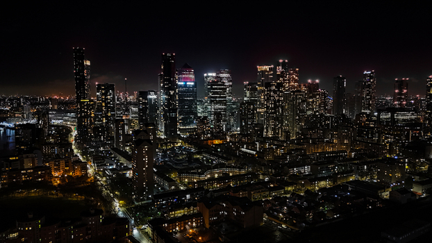 Aerial view of the illuminated Canary Wharf skyline at night with dense urban development and glowing skyscrapers in London England United Kingdom. Aerial view of the illuminated Canary Wharf skyline at night with dense urban development and glowing skyscrapers in London England United Kingdom.