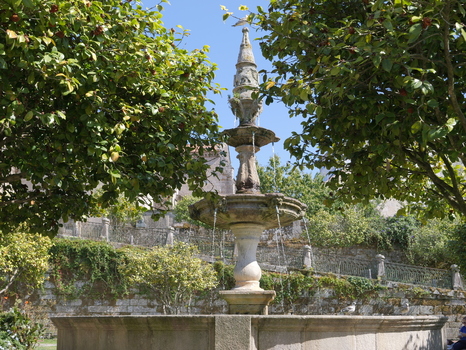 View of the historic stone fountain in Fonte Plaza de Orense framed by lush green trees and stone walls in the city center Pontevedra Pontevedra Spain. View of the historic stone fountain in Fonte Plaza de Orense framed by lush green trees and stone walls in the city center Pontevedra Pontevedra Spain.