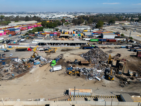 Aerial view of a scrap metal recycling yard with piles of metal heavy machinery excavators and shipping containers in Carson California United States.