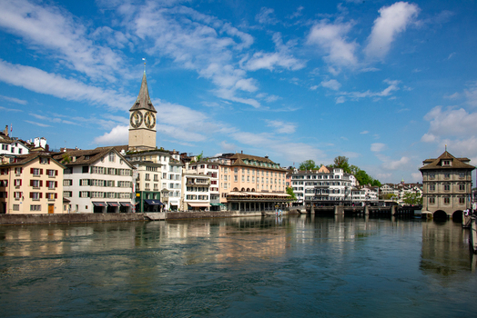 View of the St. Peter Church tower and historic buildings along the Limmat river under a blue sky in Zurich Zurich Switzerland.