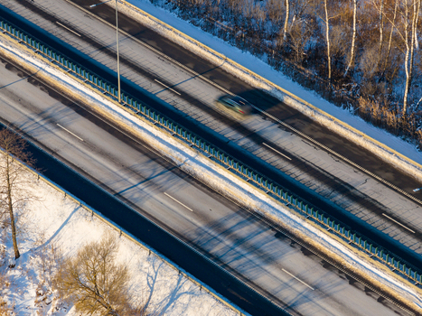 Aerial view of a multi lane highway with a car driving past snow covered embankments and bare trees in winter Lithuania. Aerial view of a multi lane highway with a car driving past snow covered embankments and bare trees in winter Lithuania.