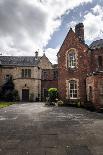 View of historic stone and brick architecture featuring arched windows a paved courtyard and a wooden bench under a cloudy sky in Newcastle upon Tyne England United Kingdom. View of historic stone and brick architecture featuring arched windows a paved courtyard and a wooden bench under a cloudy sky in Newcastle upon Tyne England United Kingdom.