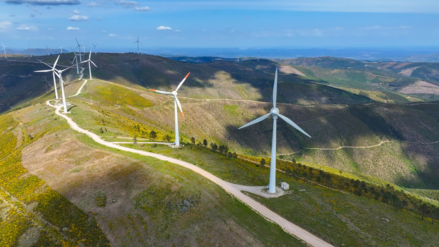 Aerial view of wind turbines situated on rolling hills with yellow vegetation and a dirt path under a clear blue sky in Lisbon Lisbon Portugal. Aerial view of wind turbines situated on rolling hills with yellow vegetation and a dirt path under a clear blue sky in Lisbon Lisbon Portugal.