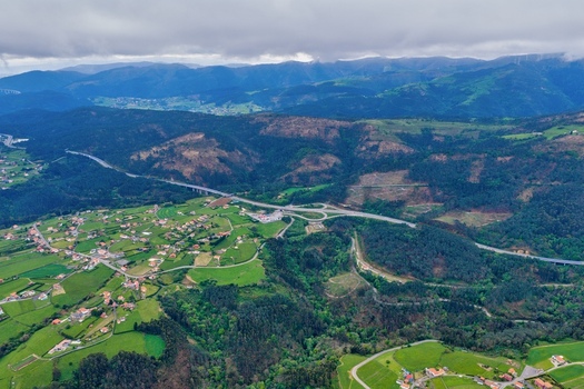 Aerial view of the lush green hills and a highway viaduct passing through a small village under a cloudy sky in Cudillero Asturias Spain.