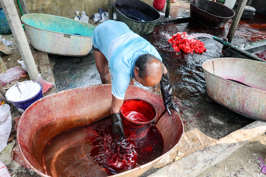 Narayanganj Bangladesh 29 March 2026 View of a worker knee deep in a crimson dye bath his gloved hands submerged surrounded by vibrant tubs of fabric a scene of intense color and labor. Narayanganj Bangladesh 29 March 2026 View of a worker knee deep in a crimson dye bath his gloved hands submerged surrounded by vibrant tubs of fabric a scene of intense color and labor.