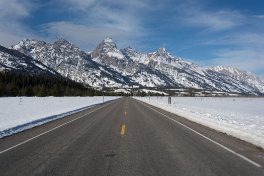 View of Jackson Hole with the snow capped Teton Range mountains rising above a paved road in Teton County Wyoming United States.