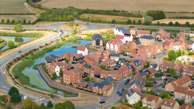 Aerial view of a modern residential housing estate with red brick houses dark roofs and winding roads situated next to a small pond and a roundabout in Bedford England United Kingdom. Aerial view of a modern residential housing estate with red brick houses dark roofs and winding roads situated next to a small pond and a roundabout in Bedford England United Kingdom.