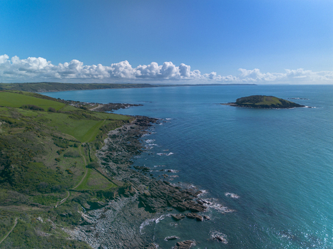 Aerial view of the rugged coastline and Looe Island near the town of Looe featuring rocky cliffs green coastal fields and the blue waters of the English Channel in Looe Cornwall United Kingdom. Aerial view of the rugged coastline and Looe Island near the town of Looe featuring rocky cliffs green coastal fields and the blue waters of the English Channel in Looe Cornwall United Kingdom.