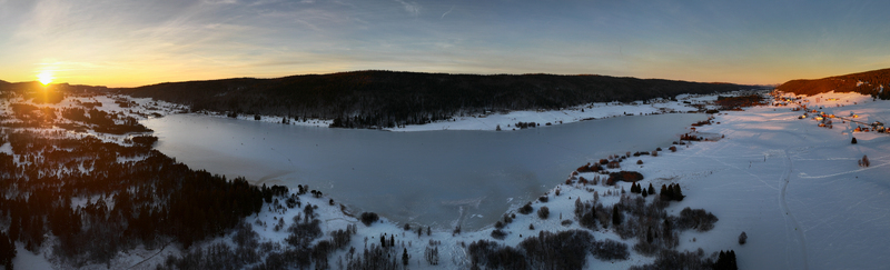 Aerial view of golden sunlight kisses the snow covered landscape and frozen lake casting long shadows over the village of Les Rousses Bourgogne Franche Comté France. Aerial view of golden sunlight kisses the snow covered landscape and frozen lake casting long shadows over the village of Les Rousses Bourgogne Franche Comté France.