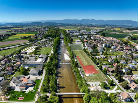 Aerial view of the Emmensteg bridge crossing the Emme river surrounded by sports fields lush green trees and residential houses Kirchberg Bern Switzerland. Aerial view of the Emmensteg bridge crossing the Emme river surrounded by sports fields lush green trees and residential houses Kirchberg Bern Switzerland.