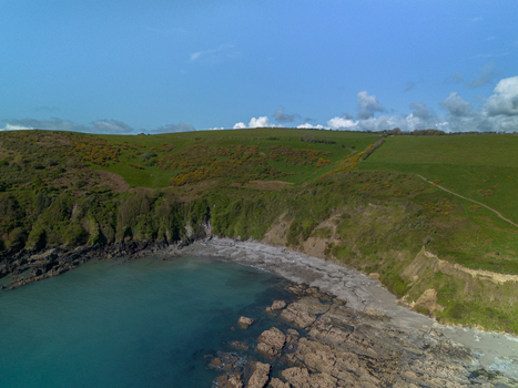 Aerial view of Portnadler Bay featuring rugged cliffs rocky shoreline and green coastal hills under a clear blue sky in Looe Cornwall United Kingdom. Aerial view of Portnadler Bay featuring rugged cliffs rocky shoreline and green coastal hills under a clear blue sky in Looe Cornwall United Kingdom.