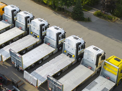 Aerial view of a row of white flatbed trucks parked in an orderly line on a paved lot in Krakow Lesser Poland Voivode Poland. Aerial view of a row of white flatbed trucks parked in an orderly line on a paved lot in Krakow Lesser Poland Voivode Poland.