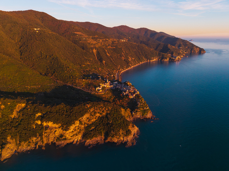 Aerial view of the village perched on a rocky cliff overlooking the Mediterranean Sea with terraced hillsides in golden sunset light Corniglia Liguria Italy. Aerial view of the village perched on a rocky cliff overlooking the Mediterranean Sea with terraced hillsides in golden sunset light Corniglia Liguria Italy.