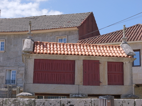 View of a traditional stone horreo with red wooden doors and a tiled roof in the historic village of Combarro Pontevedra Spain.
