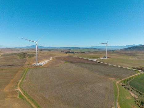 Aerial view of two large wind turbines standing in vast agricultural fields under a clear blue sky with distant mountains Swellendam Western Cape South Africa. Aerial view of two large wind turbines standing in vast agricultural fields under a clear blue sky with distant mountains Swellendam Western Cape South Africa.