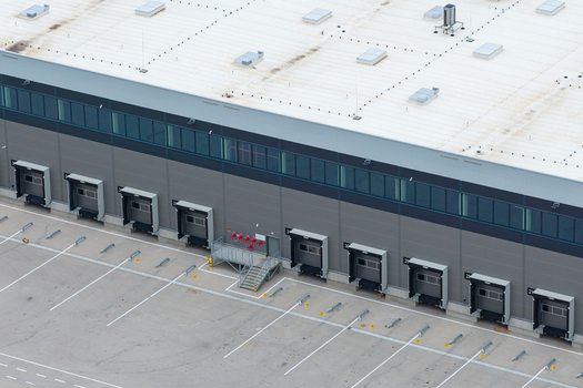 Aerial view of a large distribution hub featuring multiple loading docks a paved parking area with marked spaces and a modern industrial warehouse building in Poland. Aerial view of a large distribution hub featuring multiple loading docks a paved parking area with marked spaces and a modern industrial warehouse building in Poland.