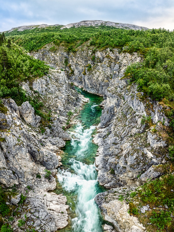 Aerial view of Silfar Canyon with a turquoise river flowing through steep rocky cliffs and lush green vegetation in Borselv Finnmark Norway.