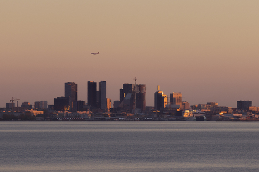 Aerial view of the Tallinn skyline at sunset with modern skyscrapers a calm sea in the foreground and an airplane flying in the warm evening sky in Tallinn Harju County Estonia.
