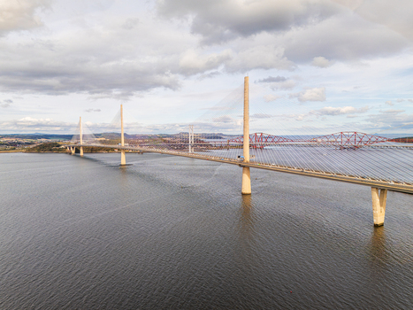 Aerial view of the Queensferry Crossing Bridge spanning the Firth of Forth with the historic Forth Bridge in the background under a cloudy sky in South Queensferry United Kingdom.