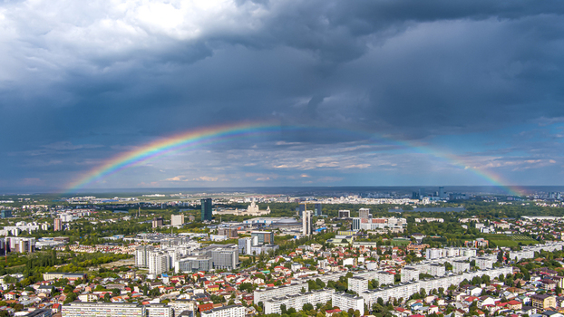Aerial view of a vibrant rainbow arching over the cityscape of Bucharest featuring residential blocks and green spaces under a dramatic stormy sky in Bucharest Bucharest Romania.
