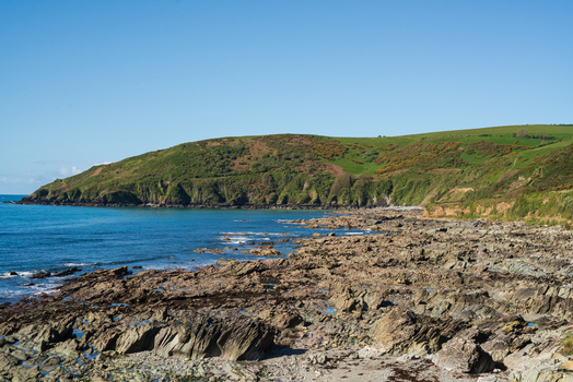 View of the rocky shoreline and green hills along the South West Coastal Path overlooking Portnadler Bay in Looe Cornwall United Kingdom. View of the rocky shoreline and green hills along the South West Coastal Path overlooking Portnadler Bay in Looe Cornwall United Kingdom.