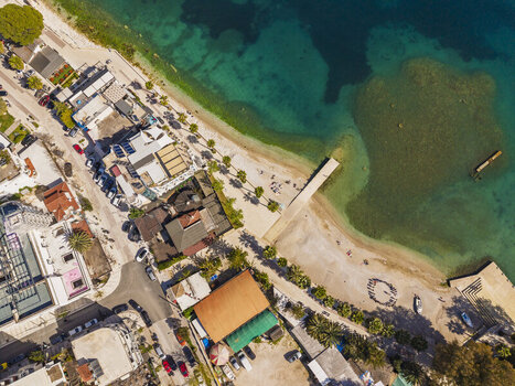 Aerial view of the coastline and beach in Saranda with palm trees buildings and a pier extending into the turquoise water in Saranda Vlore County Albania. Aerial view of the coastline and beach in Saranda with palm trees buildings and a pier extending into the turquoise water in Saranda Vlore County Albania.