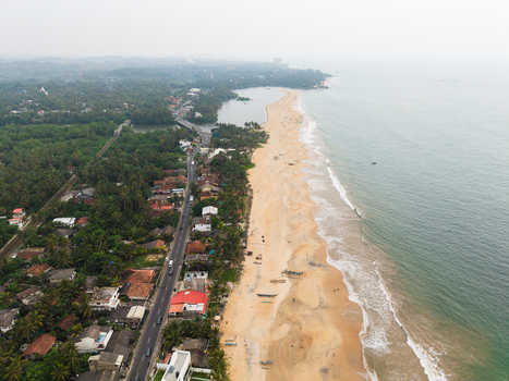 Aerial view of the sandy coastline with ocean waves lush tropical greenery and a coastal road in Galle Southern Province Sri Lanka.