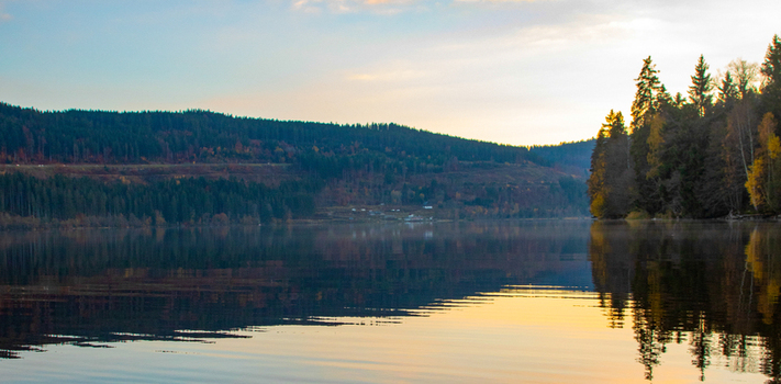 View of a still lake reflecting the dense evergreen forests of the Black Forest under a hazy sunset sky in Breitnau Baden Wurttemberg Germany. View of a still lake reflecting the dense evergreen forests of the Black Forest under a hazy sunset sky in Breitnau Baden Wurttemberg Germany.