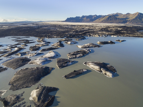 Aerial view of lake with icebergs covered with black volcanic ash in front of glacier tongue Skeidararjokull Iceland.