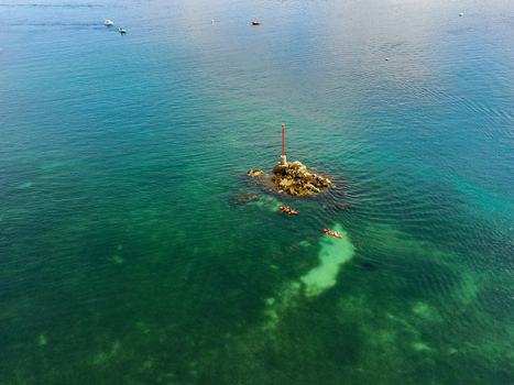 Aerial view of the red beacon on a rocky outcrop in the sea with kayakers paddling in the clear turquoise water near Ile de Brehat Brittany France.