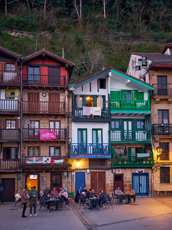 Pasai Donibane Spain 09 March 2026 View of traditional colorful houses with wooden balconies and people sitting at outdoor cafe tables in the main harbor street at dusk.