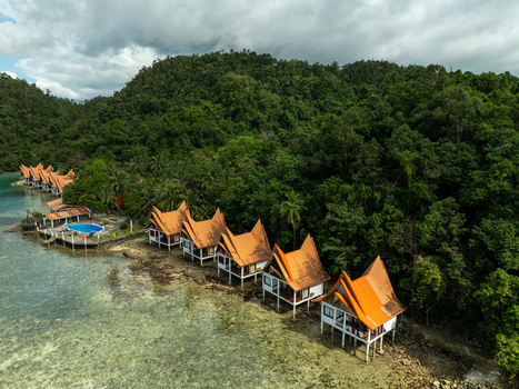 Aerial view of Bucas Grande resort featuring stilt houses with orange roofs nestled along the lush tropical coastline clear shallow water and a swimming pool in Siargao Philippines. Aerial view of Bucas Grande resort featuring stilt houses with orange roofs nestled along the lush tropical coastline clear shallow water and a swimming pool in Siargao Philippines.