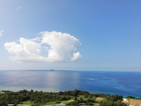 Aerial view of Sesoko Island surrounded by turquoise coral reefs and deep blue ocean waters with lush coastal greenery under a clear blue sky in Motobu Okinawa Japan. Aerial view of Sesoko Island surrounded by turquoise coral reefs and deep blue ocean waters with lush coastal greenery under a clear blue sky in Motobu Okinawa Japan.