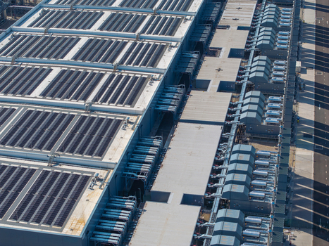 Aerial view of a large industrial datacenter featuring rows of solar panels on the roof and cooling units along the side in The Netherlands. Aerial view of a large industrial datacenter featuring rows of solar panels on the roof and cooling units along the side in The Netherlands.